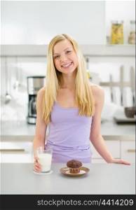 Happy teenager girl with glass of milk and chocolate muffin in kitchen
