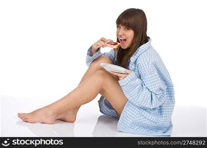 Happy teenager in pajamas eating healthy toast for breakfast on white background