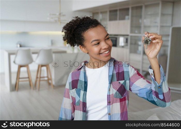 Happy teenager is homeowner in living room of new residence. Cute young african american girl is holding key from new apartment. Mortgage loan and real estate purchase conceptual image.. Happy teenager is homeowner in living room of new residence. Girl holding key from new apartment.