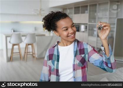 Happy teenager is homeowner in living room of new residence. Cute young african american girl is holding key from new apartment. Mortgage loan and real estate purchase conceptual image.. Happy teenager is homeowner in living room of new residence. Girl holding key from new apartment.