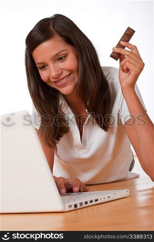 Happy teenager with laptop holding chocolate bar on wooden floor