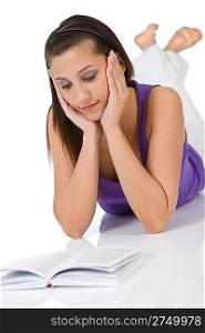 Happy teenager woman with book lying down on white background