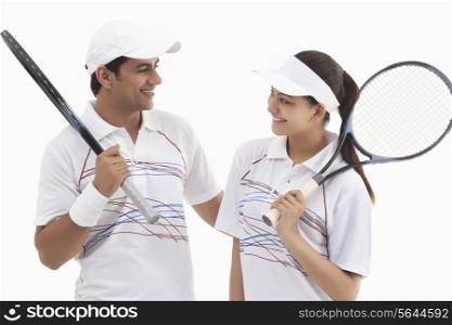Happy tennis players looking at each other while holding rackets isolated over white background