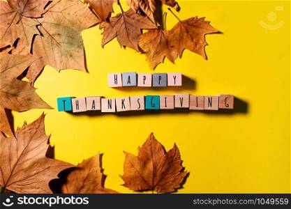 Happy Thanksgiving Day with maple leaves and wooden cube on yellow background