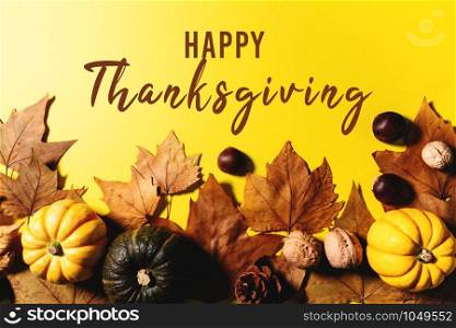 Happy Thanksgiving Day with maple leaves, nut and pumpkin on yellow background
