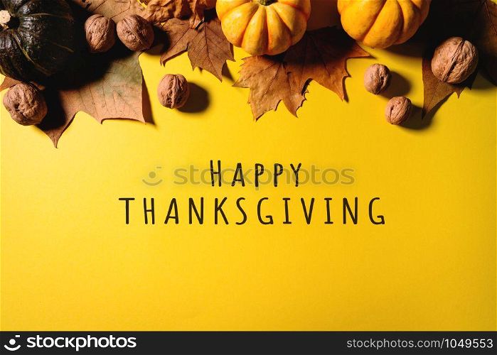 Happy Thanksgiving Day with maple leaves, nut and pumpkin on yellow background