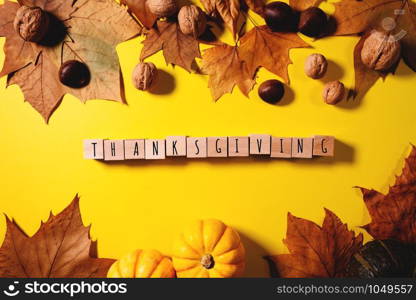 Happy Thanksgiving Day with maple leaves, nut, pumpkin and wooden cube on yellow background