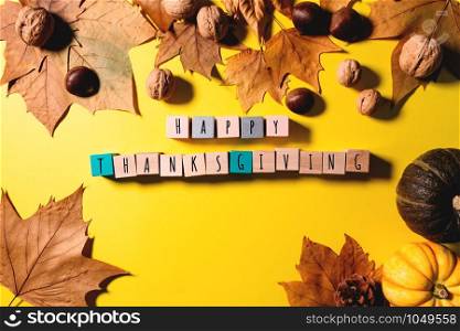 Happy Thanksgiving Day with maple leaves, nut, pumpkin and wooden cube on yellow background