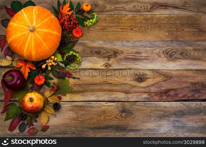 Happy Thanksgiving decor with fall leaves on wooden background. Happy Thanksgiving decor with pumpkin, apples and autumn leaves on the left side of rustic wooden table. Fall background with seasonal vegetables and fruits, copy space