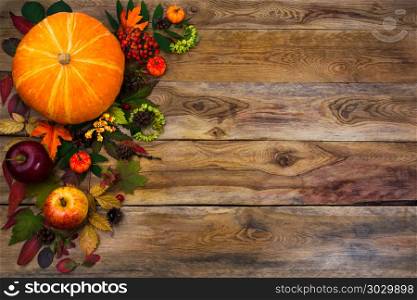Happy Thanksgiving decor with fall leaves on wooden background. Happy Thanksgiving decor with pumpkin, apples and autumn leaves on the left side of rustic wooden table. Fall background with seasonal vegetables and fruits, copy space