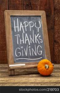 Happy Thanksgiving greeting card - white chalk handwriting on a blackboard with a pumpkin gourd agains barn wood