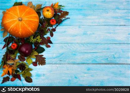 Happy Thanksgiving greeting with fall leaves on blue wooden bac. Happy Thanksgiving greeting with pumpkin, apples and autumn leaves on the left side of blue wooden table. Fall background with seasonal vegetables and fruits, copy space