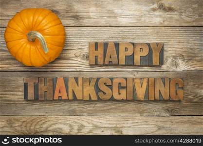 Happy Thanksgiving - text in vintage letterpress wood type blocks against rustic wood background with a pumpkin