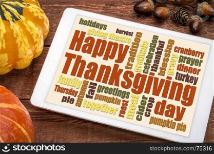 Happy Thanksgiving word cloud on a digital tablet with pumpkin and acorn decoration