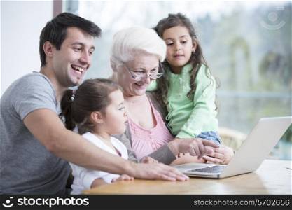 Happy three generation family using laptop at table in house