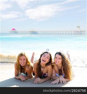 happy three teen friends girls lying on beach sand smiling at Huntington Beach California