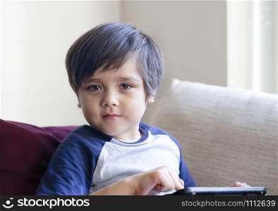 Happy toddler boy having fun playing game on teblet, Preschool kid sitting on sofa with smiling face watching cartoon on digital taplet,Child using touch padwhile relaxing at home.