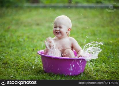 Happy toddler in a washbowl on the grass at the yard