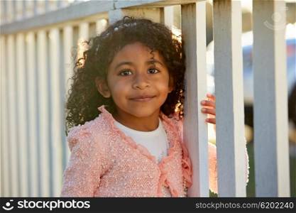 Happy toddler kid girl portrait in a park fence latin ethnicity