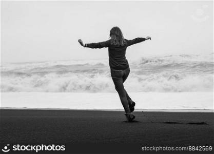 Happy tourist on black northern beach monochrome scenic photography. Picture of person with stormy sea on background. High quality wallpaper. Photo concept for ads, travel blog, magazine, article. Happy tourist on black northern beach monochrome scenic photography