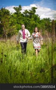 Happy traditional ukrainian couple holding hands and walking at field