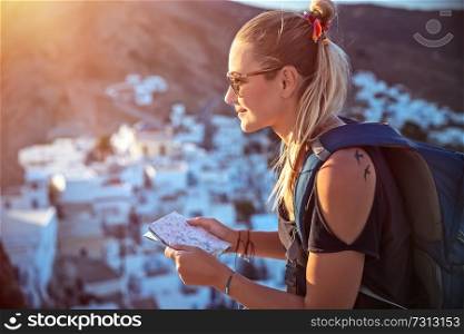 Happy traveler girl is looking to the map, searching the way to walk to beautiful city, which she sees far away in the mountains, active summer vacation with backpack