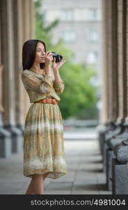 Happy traveler girl making photo of historical building with retro camera on city street