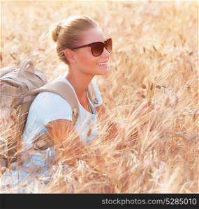 Happy traveler girl sitting with backpack in wheat field, enjoying autumn nature, tracking along Italy, travel and tourism concept