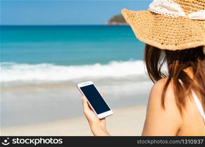 Happy traveller Asian woman enjoys at tropical beach while using smart phone on vacation. Summer on beach concept.