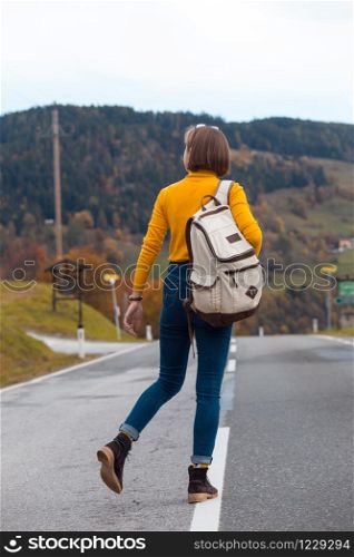 happy trip girl goes along the dividing strip road with a backpack
