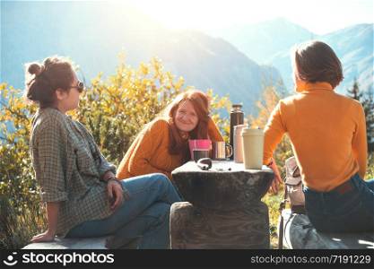 happy trip of three girls. girls have a rest and drink tea while traveling in the mountains