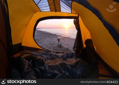 happy trip - view of the sea, camping stove, bowl, cup from the yellow tent on the beach at dawn. Ukrainian landscape at the Sea of Azov, Ukraine
