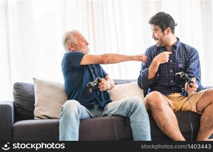 Happy two age generations men family old father embracing young grown adult son having fun enjoying video game