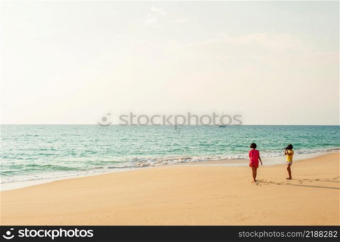 Happy two asian little girls relaxing on the sunset beach with digital camera. Holiday, Vacation concepts.