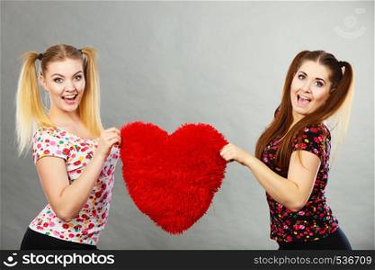 Happy two teenager women holding heart shaped pillow. Valentines day gift ideas, teenage love concept.. Happy two women holding heart shaped pillow