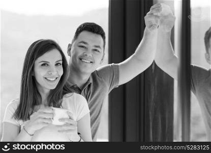 Happy two young lovers standing in living room and smiling while drinking coffe