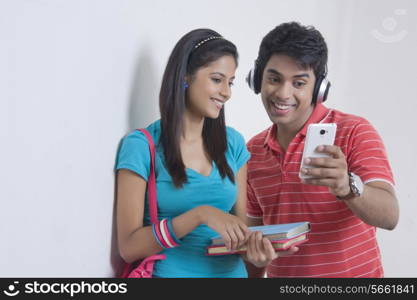 Happy university friends reading text message on smart phone against wall