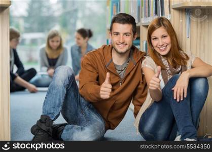 Happy university students showing thumb up with friends in library