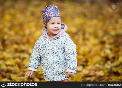 Happy urban little girl walking in city autumn park. Cute baby girl among the golden autumn maple leaves