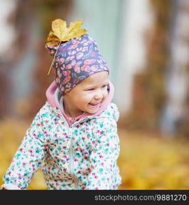 Happy urban little girl walking in city autumn park. Cute baby girl among the golden autumn maple leaves