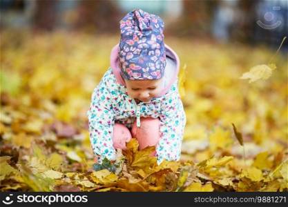 Happy urban little girl walking in city autumn park. Cute baby girl among the golden autumn maple leaves