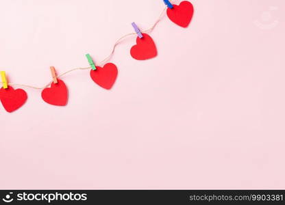 Happy Valentine’s day background. red heart shaped valentines decoration hanging with paper clips on the rope for love composition greeting card isolated on pink background with copy space