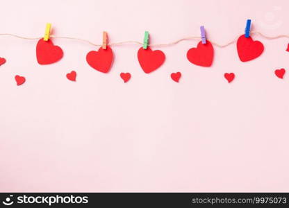 Happy Valentine’s day background. red heart shaped valentines decoration hanging with paper clips on the rope for love composition greeting card isolated on pink background with copy space