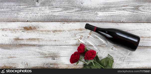 Happy Valentines Day celebration with red roses, drinking glasses and a bottle of wine on white rustic wooden background