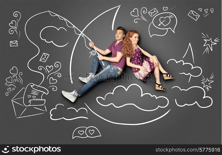 Happy valentines love story concept of a romantic couple fishing on a moon with a paper letter on a hook against chalk drawings background.