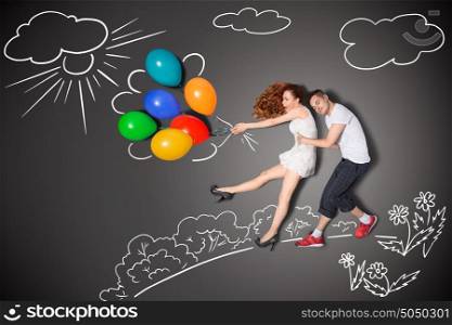 Happy valentines love story concept of a romantic couple holding balloons blowing with the wind against chalk drawings background.