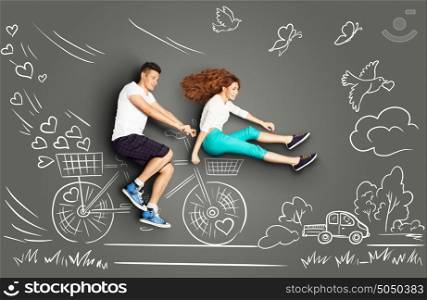 Happy valentines love story concept of a romantic couple on chalk drawings background of a countryside. Male riding his girlfriend in a front bicycle basket.