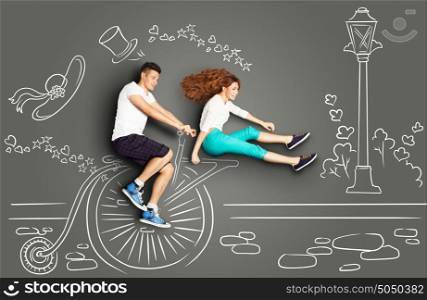 Happy valentines love story concept of a romantic couple on chalk drawings background. Male riding his girlfriend on a vintage penny-farthing bicycle.