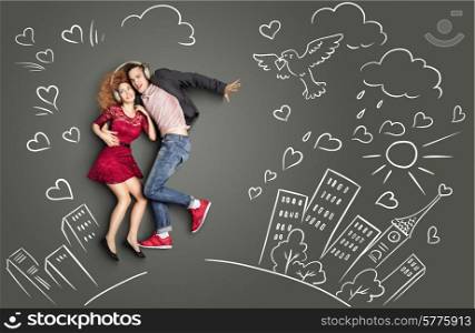 Happy valentines love story concept of a romantic couple sharing headphones and listening to the music against chalk drawings urban background.