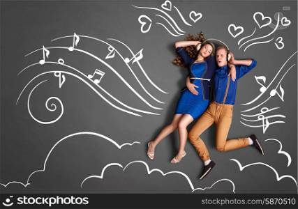 Happy valentines love story concept of a romantic couple sharing headphones and listening to the music against chalk drawings background of notes, player icons and clouds.